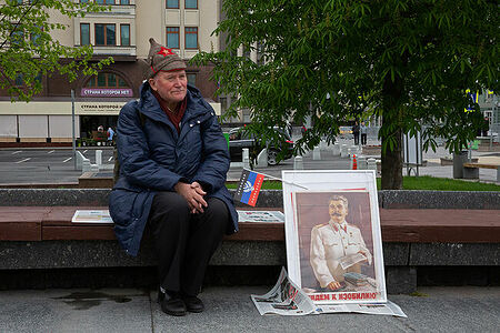 01.05.2023, Москва. Встреча депутатов фракции КПРФ с избирателями в формате патриотического митинга возле памятника Карлу Марксу. Пожилой мужчина в будёновке сидит на скамейке рядом с портретом Иосифа Сталина.