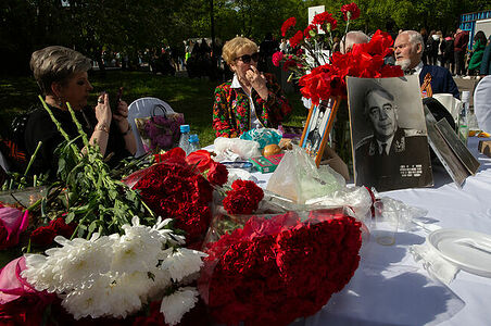 09.05.2023, Москва, Парк Горького, День Победы. Люди сидят за столом, на котором лежат букеты цветов и стоят фотографии ветеранов войны.
