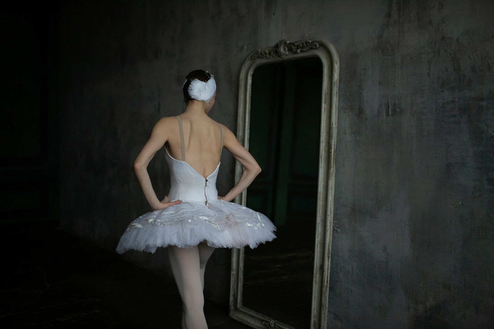 Ballerina in a swan costume stands and looks in the mirror